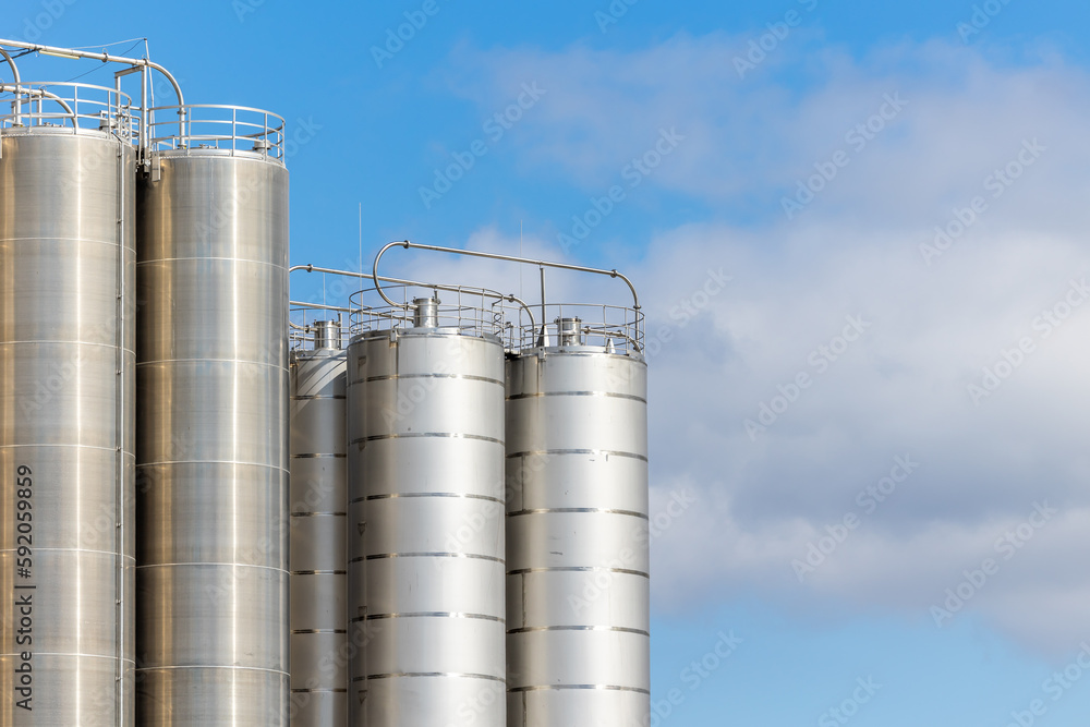 Stainless steel silos against the blue sky. Warehouses for storage of plastics and bulk grains.