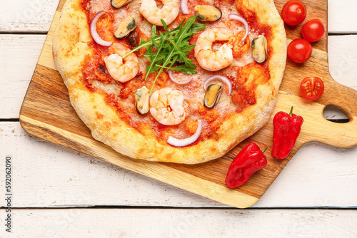 Board with tasty seafood pizza on light wooden background, closeup