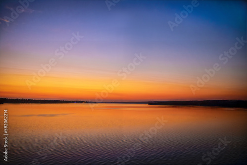 Minimalist Sunset over the lake with reflections in water and a few lights visible on far shore