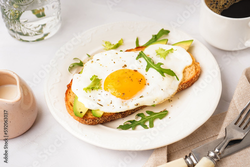 Delicious sandwich with fried egg  avocado and arugula on light background