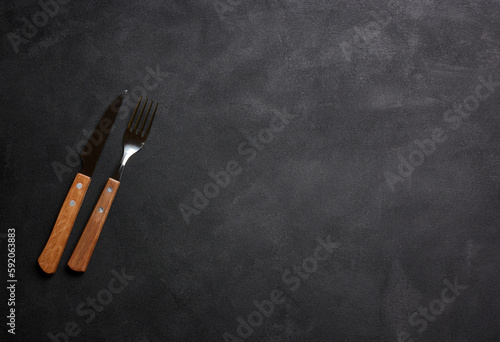 Fork and knife with wooden handle on black background, top view
