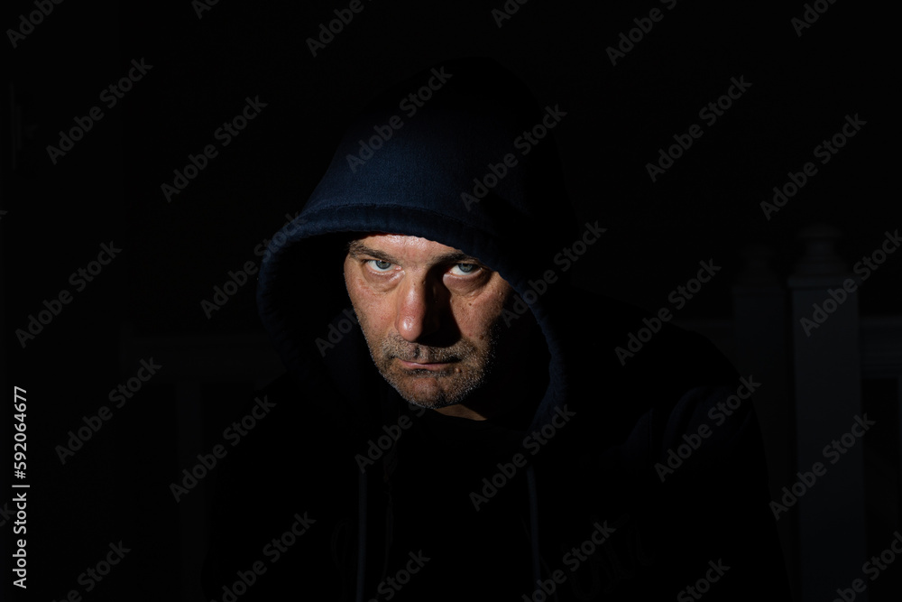 Bearded mid aged male wearing a hood in a dark room Bearded mid aged male wearing a hood in a dark room