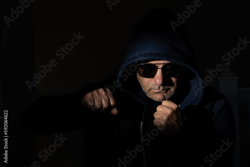 Men with unkempt facial hair and sunglasses, donning hoods, making a threatening gesture as if indicating a willingness to engage in a physical altercation within a dimly lit room.