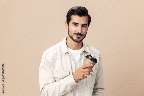 Portrait of a stylish man with a glass of coffee with himself mockup on a beige background in a white t-shirt, fashionable clothing style, space space