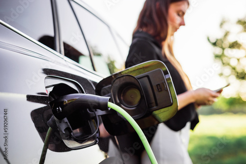 фотографія Girl charging electric car parked in the nature area and adjusting an EV chargin