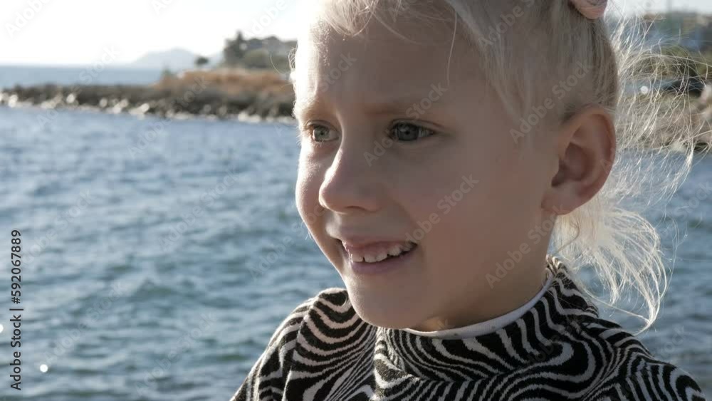 Portrait of blonde caucasian little girl with double pigtails on sea background. Child is surprised and frightened. Close-up Portrait of blonde caucasian little girl with double pigtails on sea background. Child is surprised and frightened. Close-up