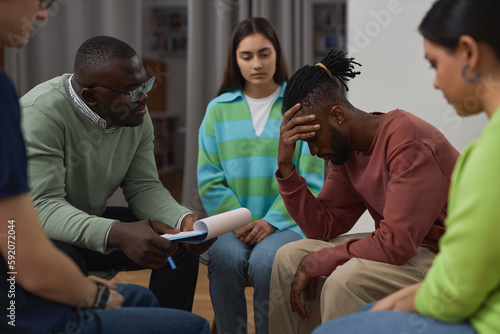 Side view portrait of troubled black man crying in support group circle and sharing story with therapist