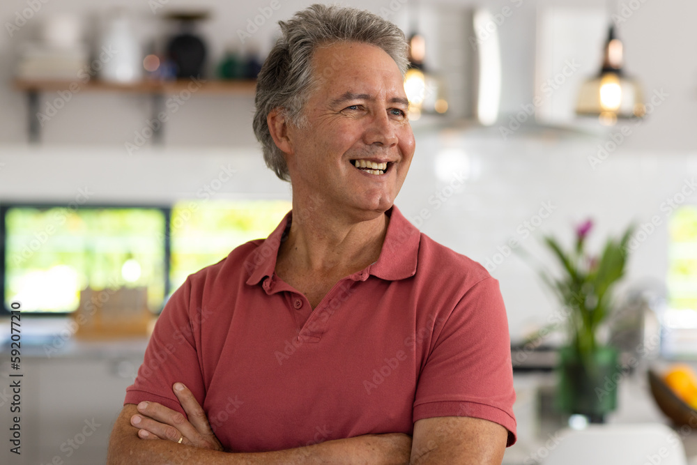 Smiling caucasian senior man with arms crossed looking away while standing at home, copy space Smiling caucasian senior man with arms crossed looking away while standing at home, copy space