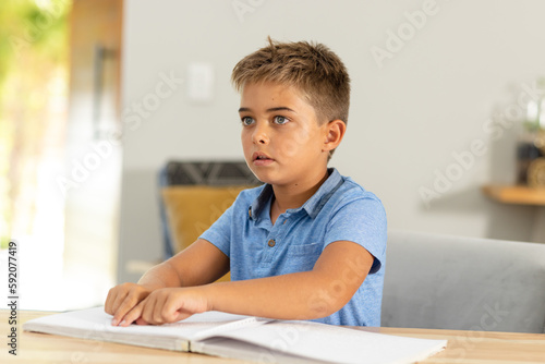 Caucasian cute blind boy reading braille book on table while sitting at home, copy space