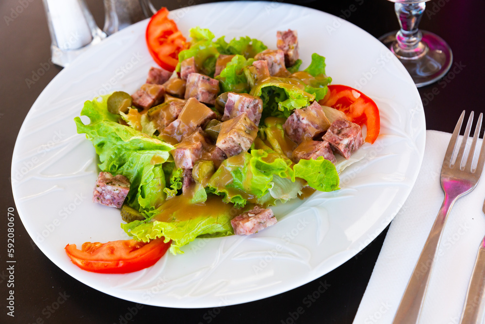 Portion of salad with headcheese, lettuce, marinated cucumbers and sauce vinaigrette, traditional french cuisine