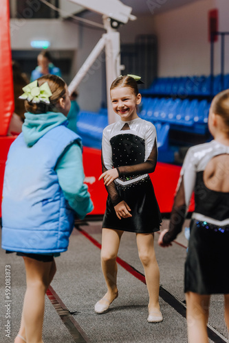 Fototapeta Naklejka Na Ścianę i Meble -  A beautiful smiling girl, a child, a cheerleader sportswoman in a uniform, a colored dress, trains in the gym. Photography, portrait, sport concept.