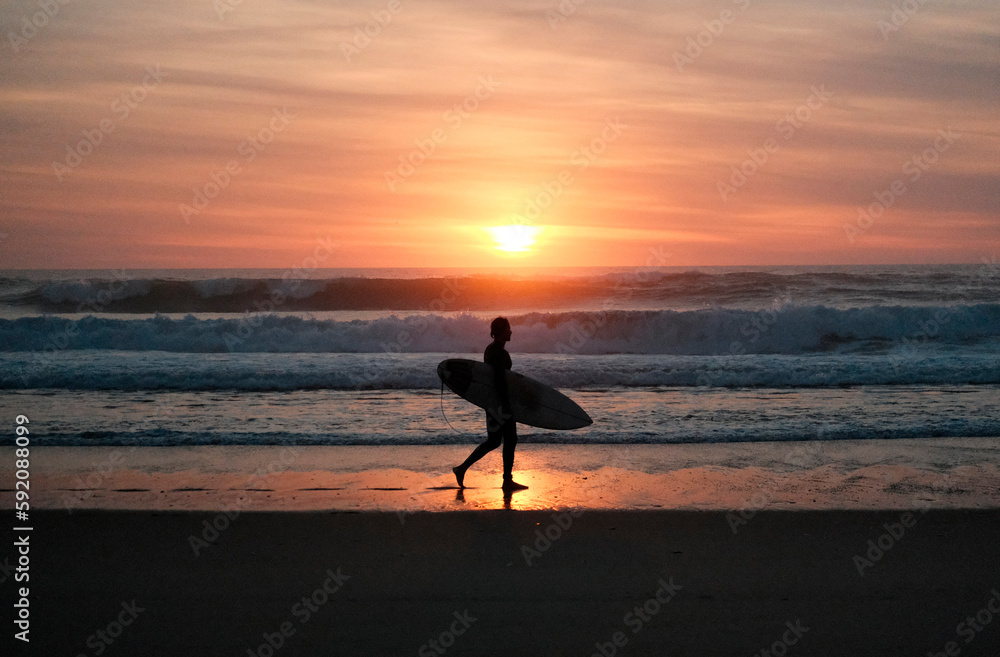 silhouette of a surfer with a surfboard walking on the beach during sunset