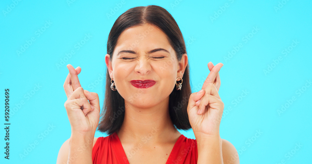 Happy, woman and face with fingers crossed on blue background, studio and wishing for good luck. Portrait of excited female model hope for winning prize, optimism and smile for emoji, hands and sign Happy, woman and face with fingers crossed on blue background, studio and wishing for good luck. Portrait of excited female model hope for winning prize, optimism and smile for emoji, hands and sign