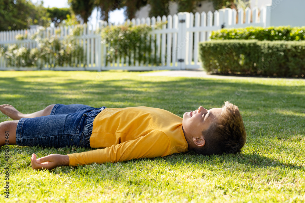 Smiling caucasian boy lying down over grassy land while relaxing in yard Smiling caucasian boy lying down over grassy land while relaxing in yard