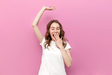 young tired sleepy woman yawns and stretches on pink isolated background, the concept of insomnia