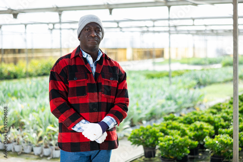 Portrait of smiling african man gardener standing at the greenhouse with flowers on background