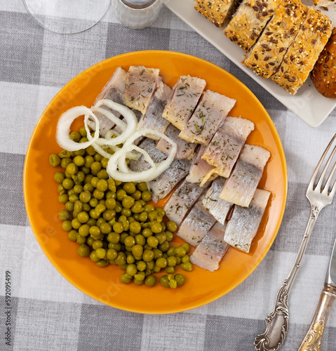 Delicious sliced herring, sprinkled with herbs on top, with canned green peas and onions, cut into rings photo