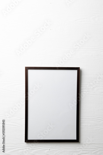 Vertical of empty dark wooden frame with copy space on white wall