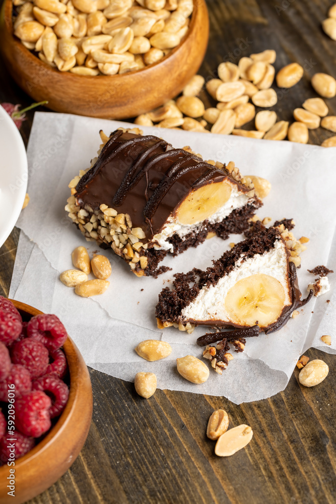 Fototapeta premium Sliced sweet cake with banana, chocolate glaze, milk filling and peanuts
