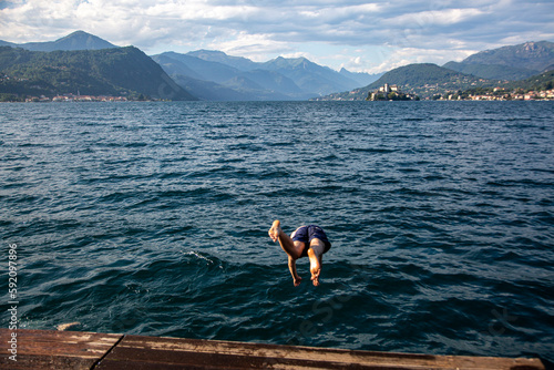 A man dives into the water in front of a mountain.