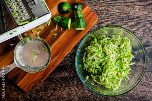 Shredded Zucchini in a Glass Mixing Bowl: Grated zucchini shown with a mandoline and other tools photo
