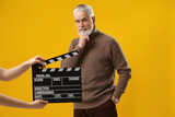 Senior actor performing while second assistant camera holding clapperboard on yellow background. Film industry