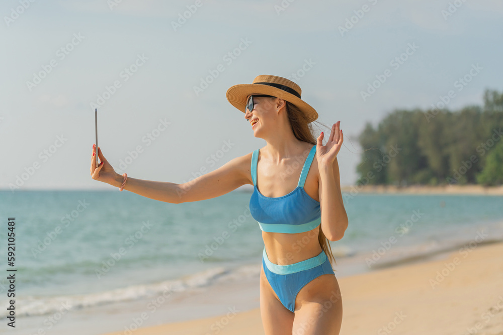 Beautiful caucasian woman using digital tablet at the beach. Female digital nomad working from the beach using her digital tablet. Sexy white woman in bikini. Workcation.