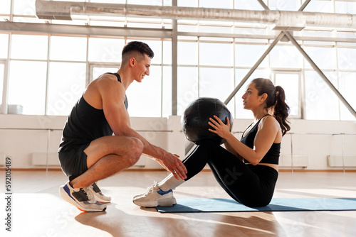 athletic couple in sportswear train with ball in the morning, fitness girl does exercise on the press with trainer