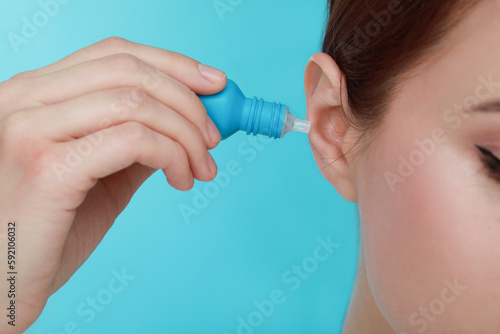 Woman using ear drops on light blue background, closeup