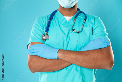 Doctor or medical assistant (male nurse) in uniform with stethoscope on turquoise background, closeup