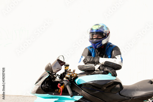 guy motorcyclist in professional protective equipment and helmet stands near sports motorcycle against white wall