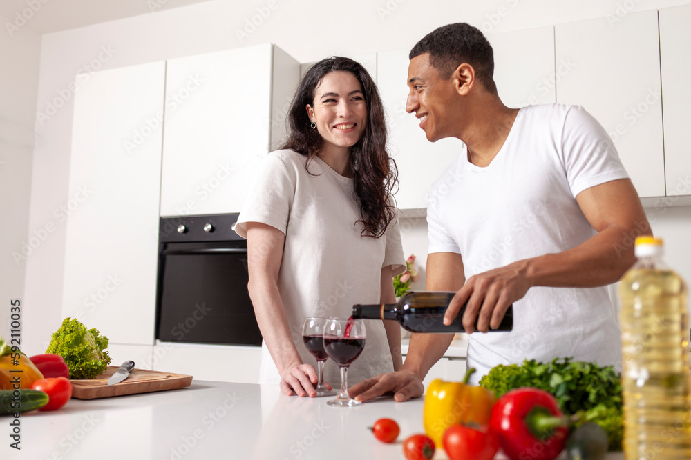young happy multiracial couple drinking wine in white modern kitchen, african american guy pouring red wine young happy multiracial couple drinking wine in white modern kitchen, african american guy pouring red wine
