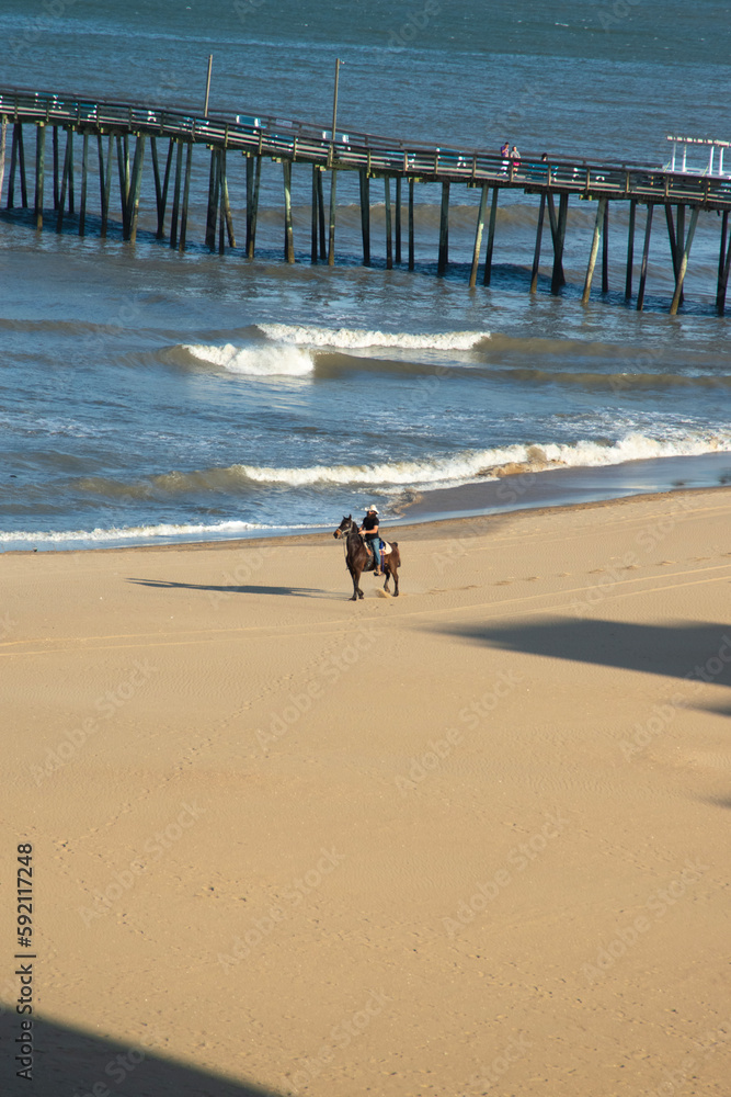 Horseback riding on the beach with a wooden pier in the background. Horseback riding on the beach with a wooden pier in the background.
