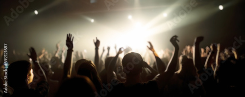 A crowd of people at a live event, concert or party hands in the air. Large audience, crowd, or participants of a live event, in a concert hall type venue with bright lights above. Generative AI.