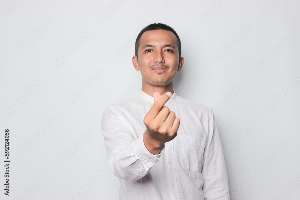 Smiling Asian young man wearing brown shirt with love hand symbol isolated on white background. Smiling Asian young man wearing brown shirt with love hand symbol isolated on white background.