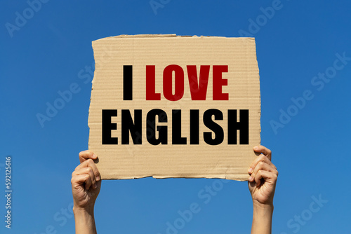 I love English text on box paper held by 2 hands with isolated blue sky background. This message board can be used as business concept about English.