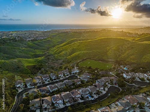 Cul de sac street surrounded by luxury two story single family homes green rolling hills in new residential West Coast USA real estate suburban neighborhood dramatic colorful sunset sky view to ocean