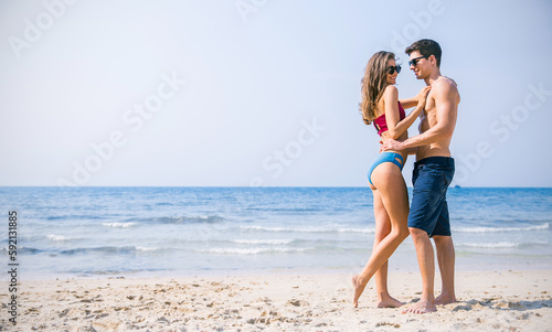 Portrait of beautiful couple of caucasian woman with man wearing sunglasses swim suit walk on beach. Young couple enjoy honeymoon after marriage at sea. Happy casual lover hold at tropical beach.