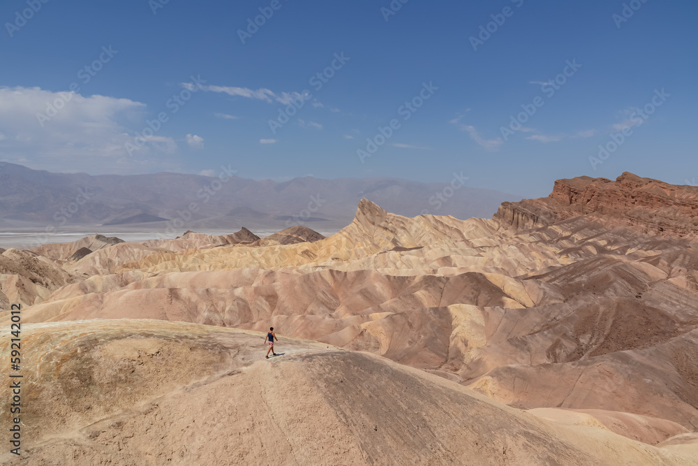 Fototapeta premium Man with scenic view of summit peak Manly Beacon seen from Zabriskie Point, Badlands, Furnace creek, Death Valley National Park, California, USA. Erosional landscape of Amargosa Chaos rock formation