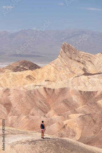 Man with scenic view of summit peak Manly Beacon seen from Zabriskie Point, Badlands, Furnace creek, Death Valley National Park, California, USA. Erosional landscape of Amargosa Chaos rock formation