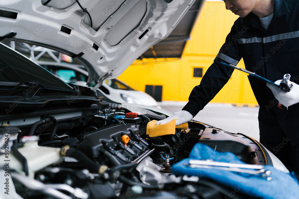 Fototapeta premium Automobile mechanic repairman checking a car engine by inspecting and writing to the clipboard the checklist for repair machine and car service for maintenance and maintenance check concept.