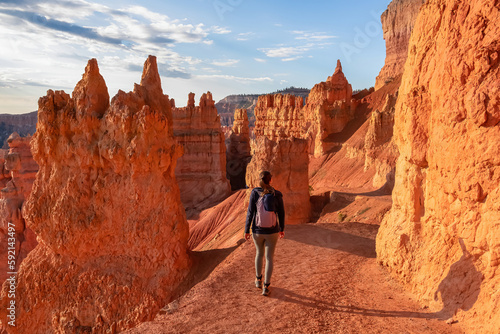 Woman in front of Thors Hammer during sunrise on Navajo Rim hiking trail Bryce Canyon National Park, Utah, USA. Scenic golden hour view of sandstone hoodoos rock formation in amphitheatre on sunny day