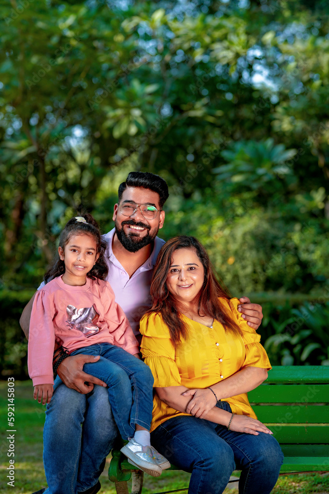 Happy Young indian parents with their cute little daughter sitting at park or garden. Happy Young indian parents with their cute little daughter sitting at park or garden.