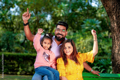 Happy Young indian parents with their cute little daughter sitting at park or garden. © Niks Ads