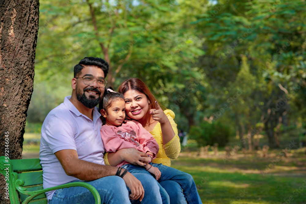 Happy Young indian parents with their cute little daughter sitting at park or garden. Happy Young indian parents with their cute little daughter sitting at park or garden.