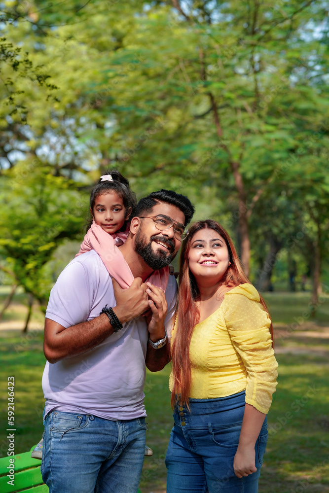 Happy Young indian parents with their cute little daughter sitting at park or garden. Happy Young indian parents with their cute little daughter sitting at park or garden.