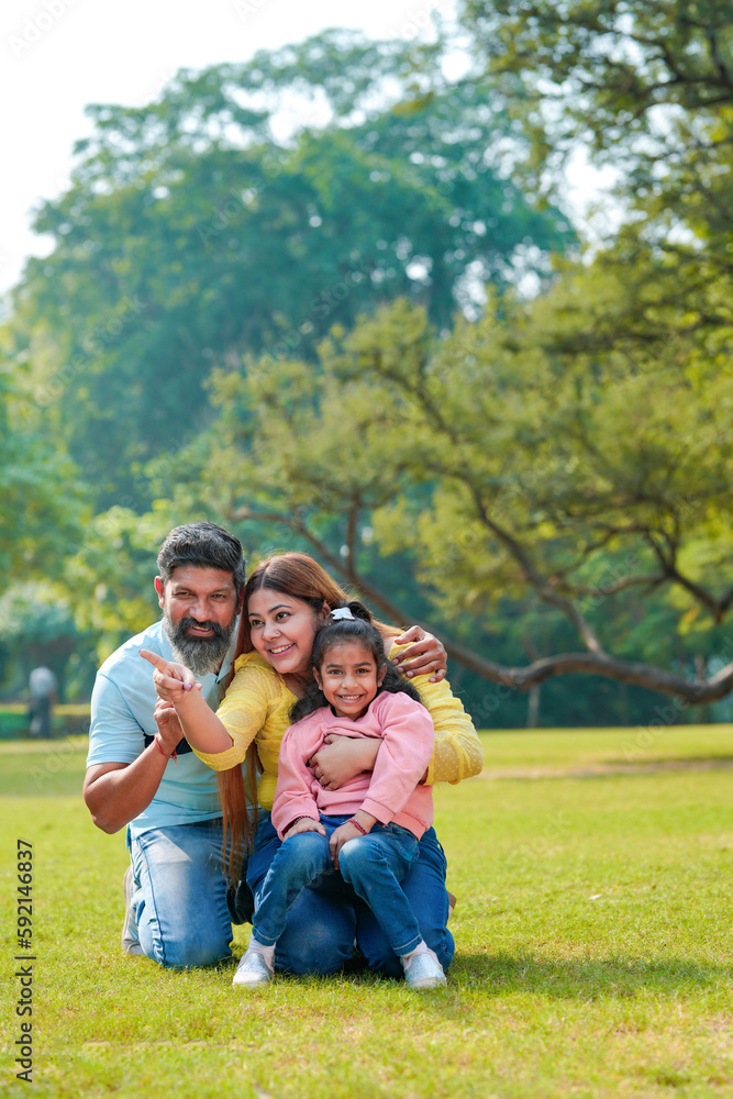 Happy Young indian parents with their cute little daughter sitting at park or garden. Happy Young indian parents with their cute little daughter sitting at park or garden.