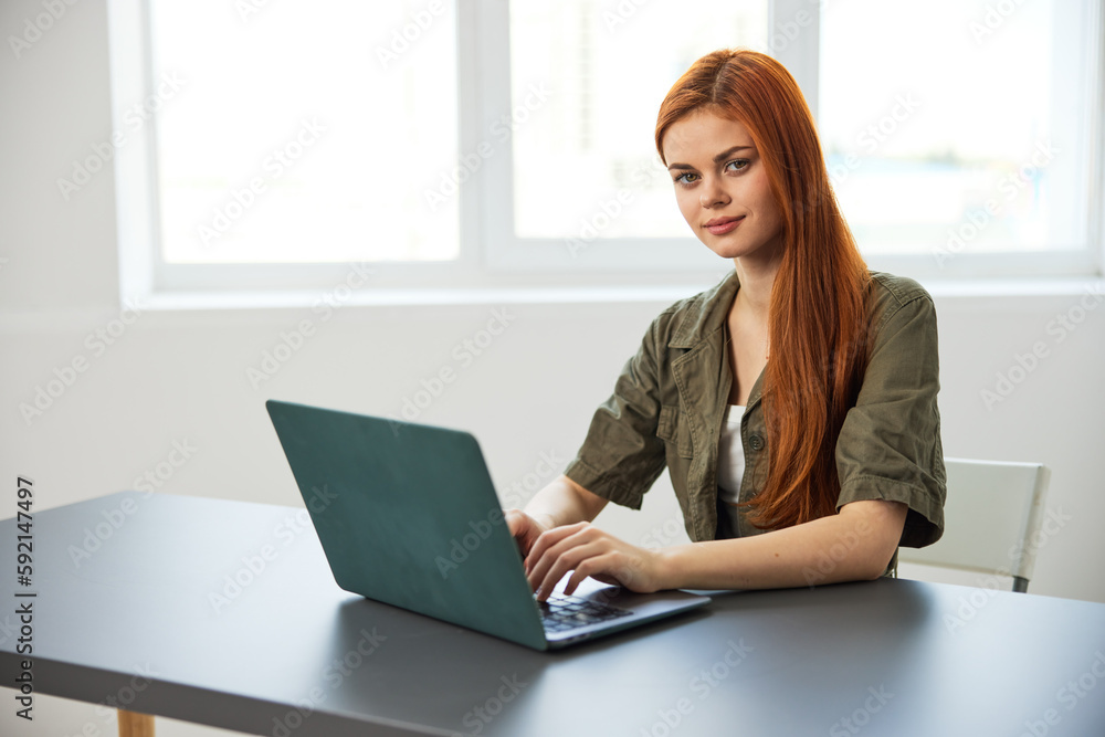 red-haired woman smiling thoughtfully sitting at work at a laptop red-haired woman smiling thoughtfully sitting at work at a laptop