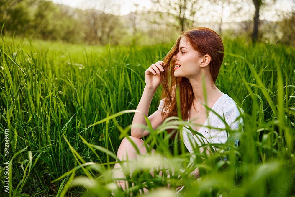 a young woman sitting resting in the tall grass straightening her hair a young woman sitting resting in the tall grass straightening her hair