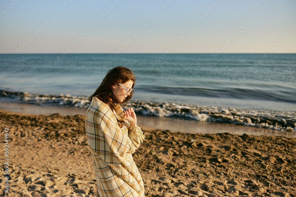 pensive woman wrapped in a blanket stands against the backdrop of the sea